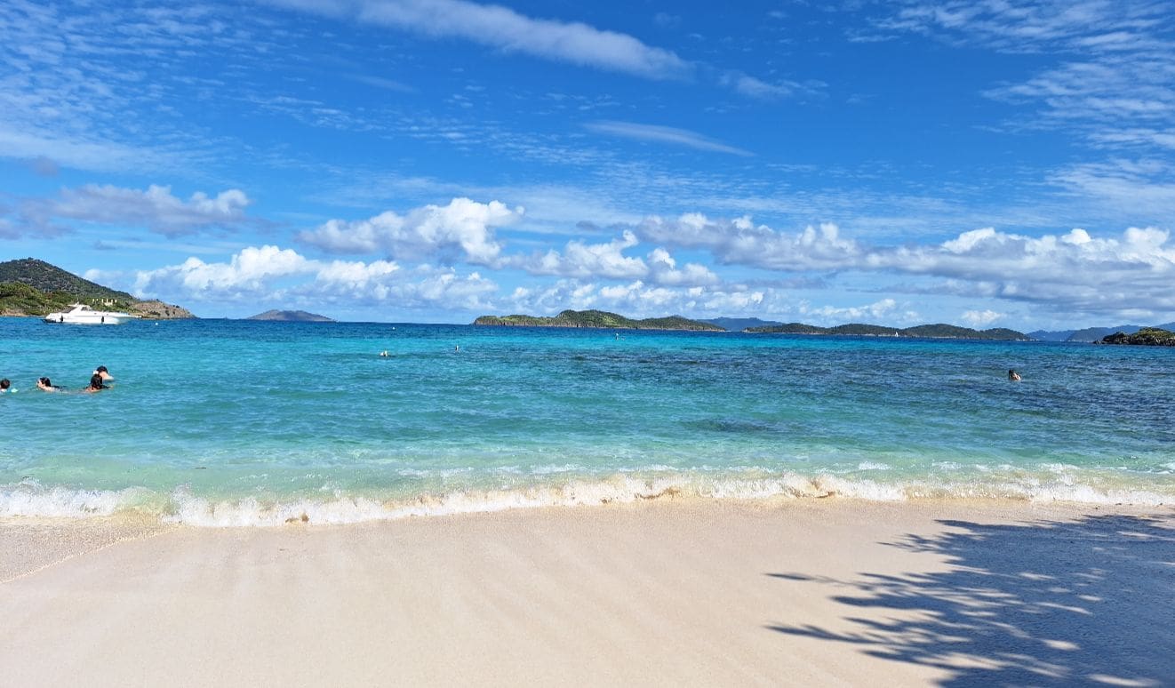 Clear blue ocean waves gently lap onto a sandy beach under a bright sky.