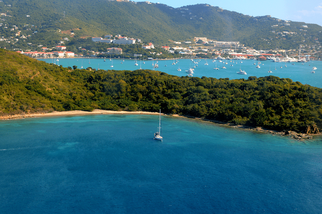 A sailboat anchored near a lush green coastline with hills in the background.