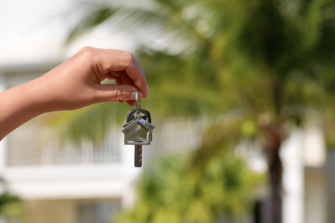 Hand holding a small house keychain with a key outdoors.