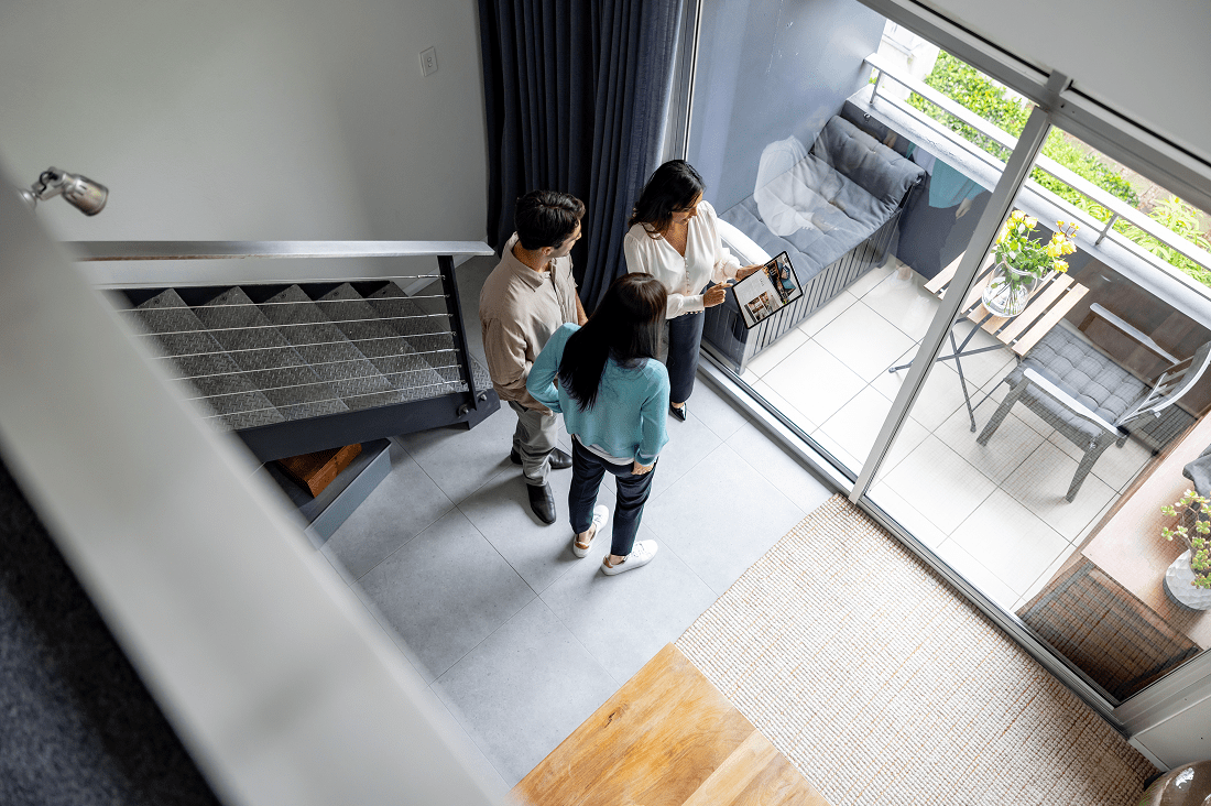 Two women wearing masks standing inside a modern apartment near a bed.